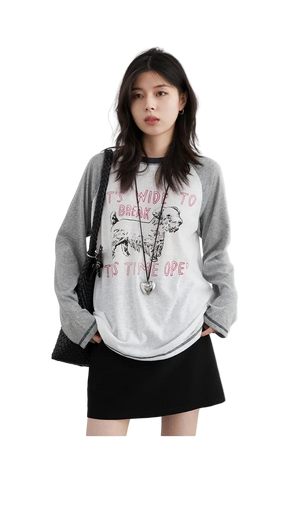 Woman wearing a gray and white graphic t-shirt with text and a graphic design.