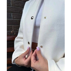 Close-up of a person wearing a white coat with gold buttons, standing against a brick wall.