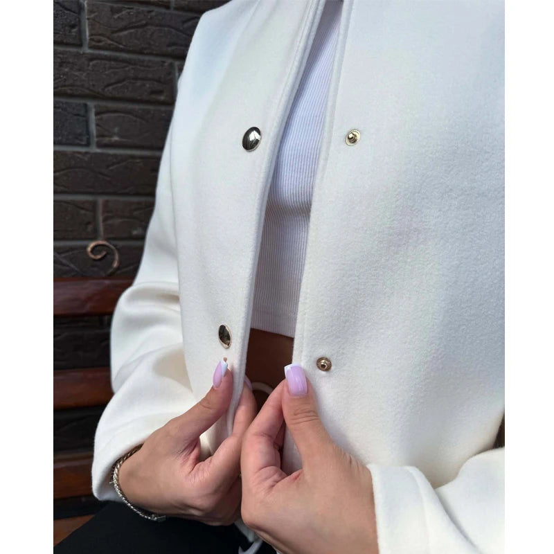 Close-up of a person wearing a white coat with gold buttons, standing against a brick wall.