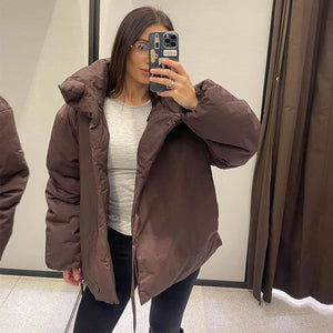 Person wearing a brown puffer jacket taking a mirror selfie.