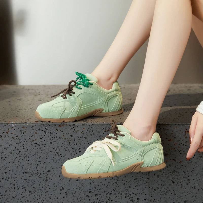 Light green sneakers with brown soles worn by a person sitting on a concrete step.