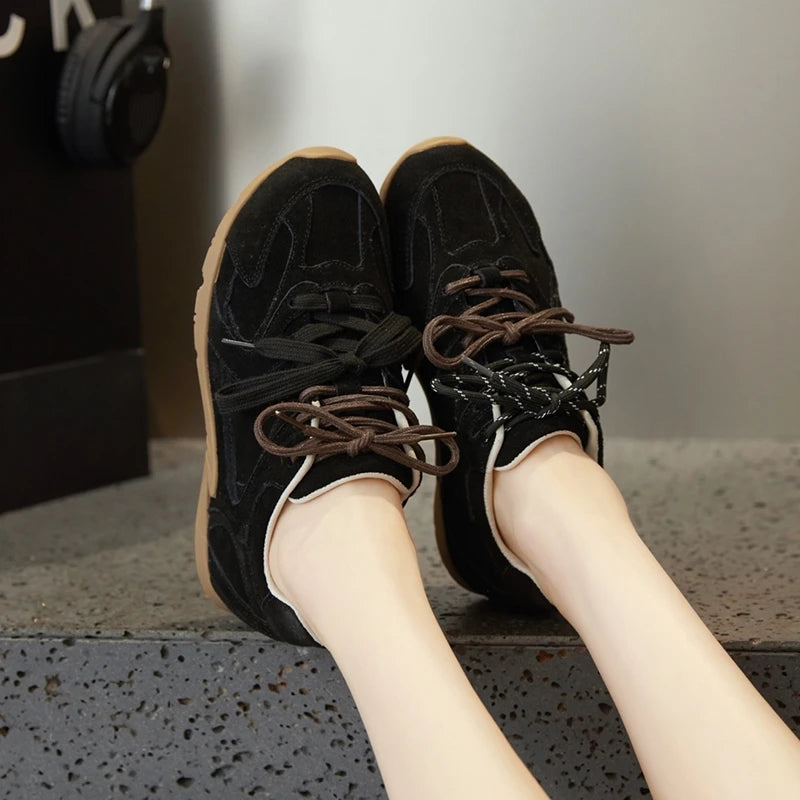 Black sneakers with brown laces worn by a person sitting on a concrete surface.