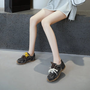 Person wearing black sneakers with white laces on a concrete surface.