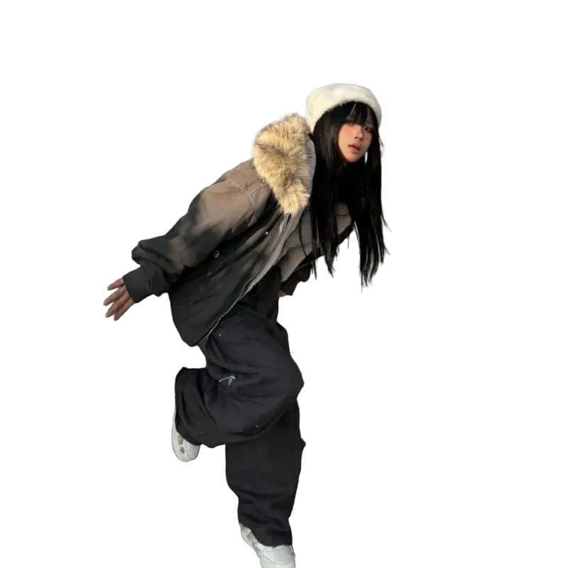 Person wearing a large fur-lined coat and black pants leaning against a building.