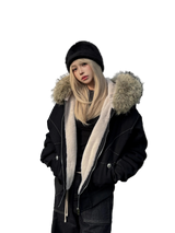 Person wearing a black coat with fur-lined hood and a black beanie outdoors.