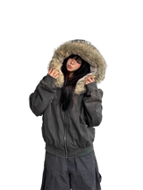 Person wearing a dark gray jacket with a fur-lined hood against a white wall.